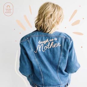 Cara Dumaplin wearing jean jacket embroidered with the words 'tough as a mother' in script font